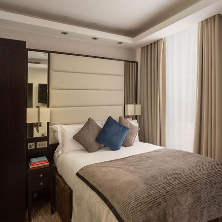 Отель Montcalm Brewery Townhouse Лондон Экстерьер фото The image shows a cozy bedroom. It features a comfortable double bed with a light-colored duvet and decorative pillows in shades of blue and gray. The headboard is upholstered in a soft material, and there are bedside lamps on either side of the bed.