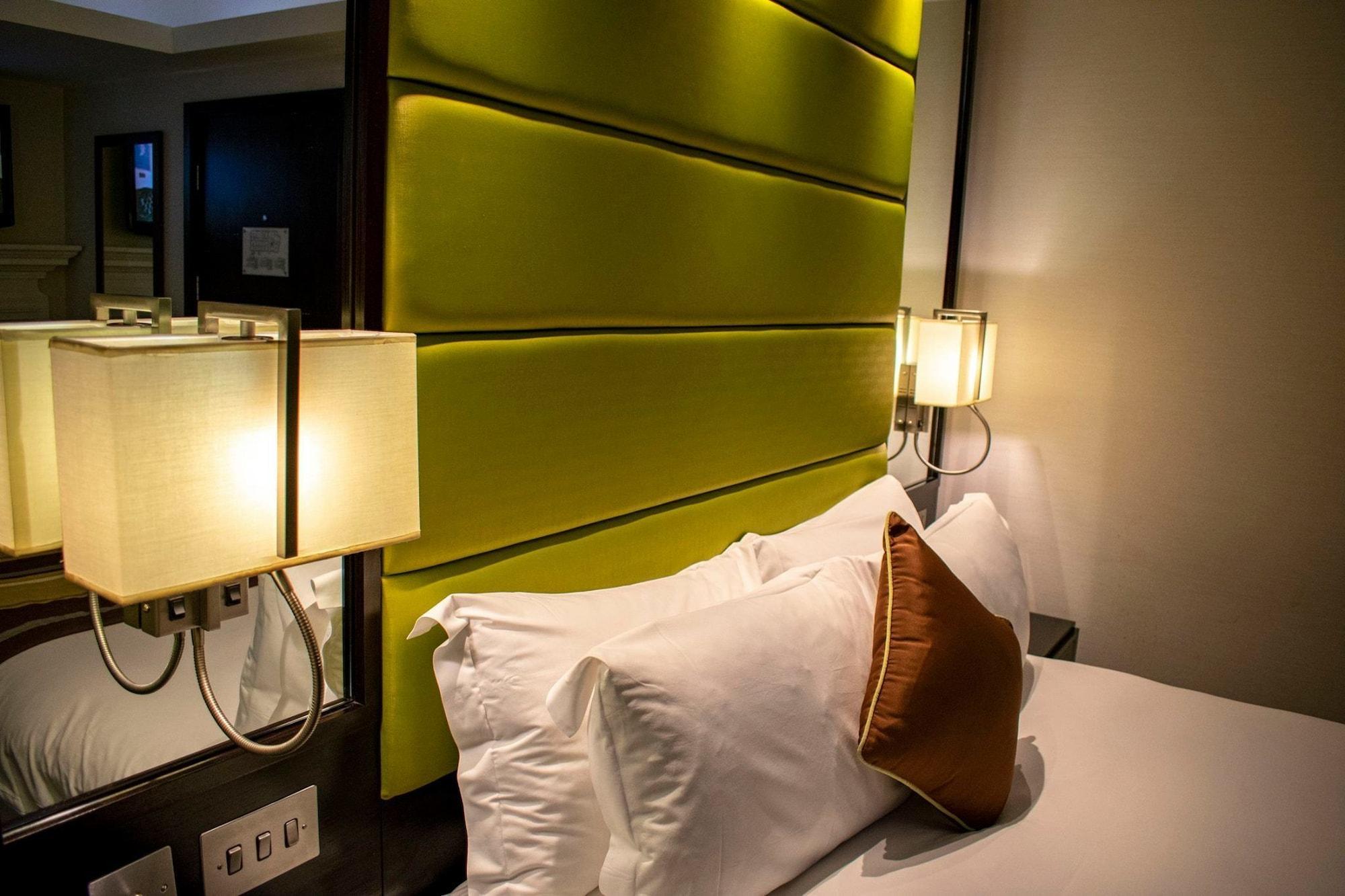 Отель Montcalm Brewery Townhouse Лондон Экстерьер фото The photo shows a modern hotel room with a stylish design. The focal point is a large bed with white pillows and a decorative brown pillow. The headboard is bright green and has a textured appearance. On either side of the bed, there are wall lamps t