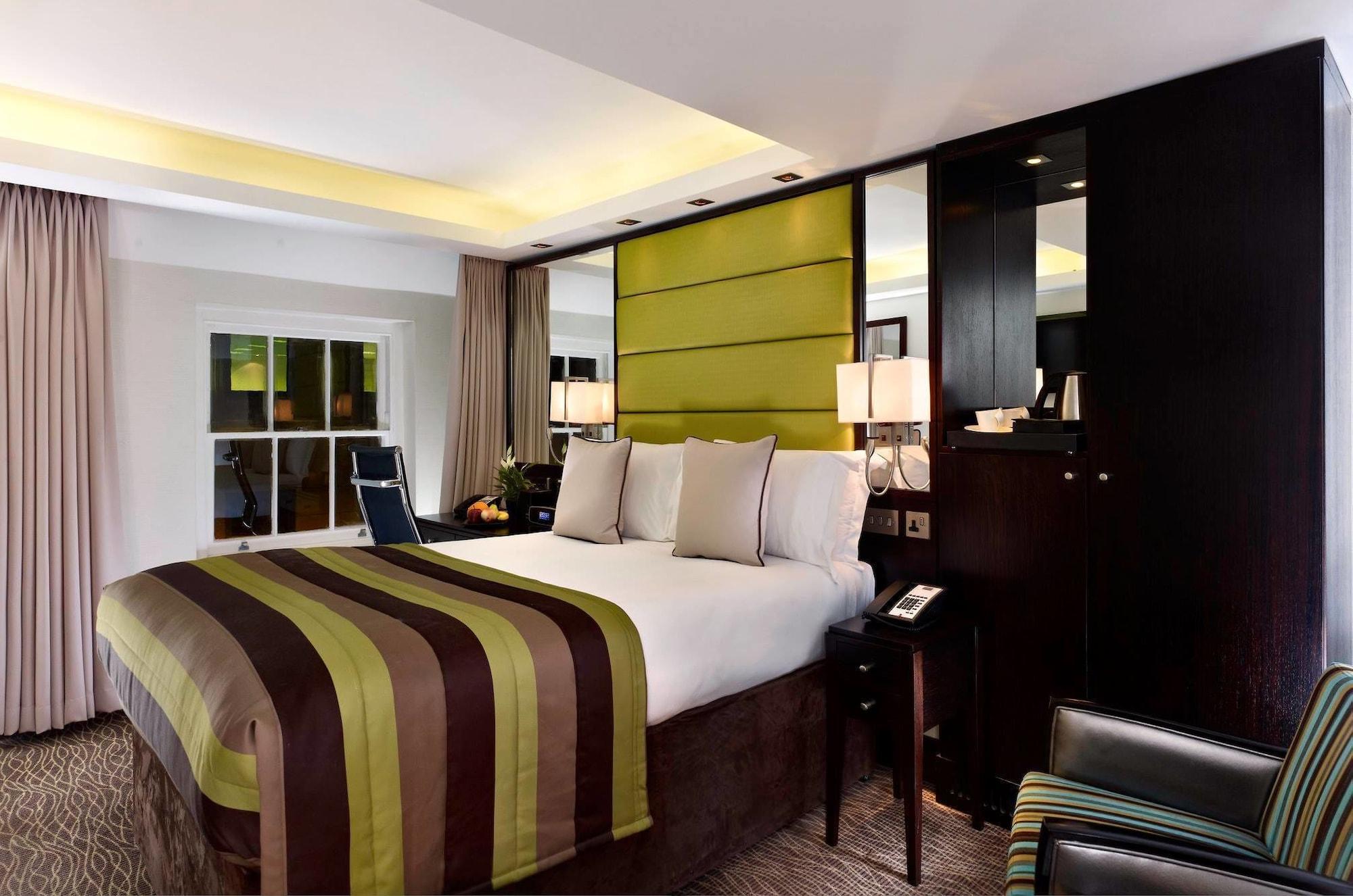 Отель Montcalm Brewery Townhouse Лондон Экстерьер фото The photo shows a modern hotel room featuring a large bed with a striped comforter in shades of green, brown, and cream. The bed is adorned with several decorative pillows. Behind the bed, there is a contemporary headboard with a green panel design. 