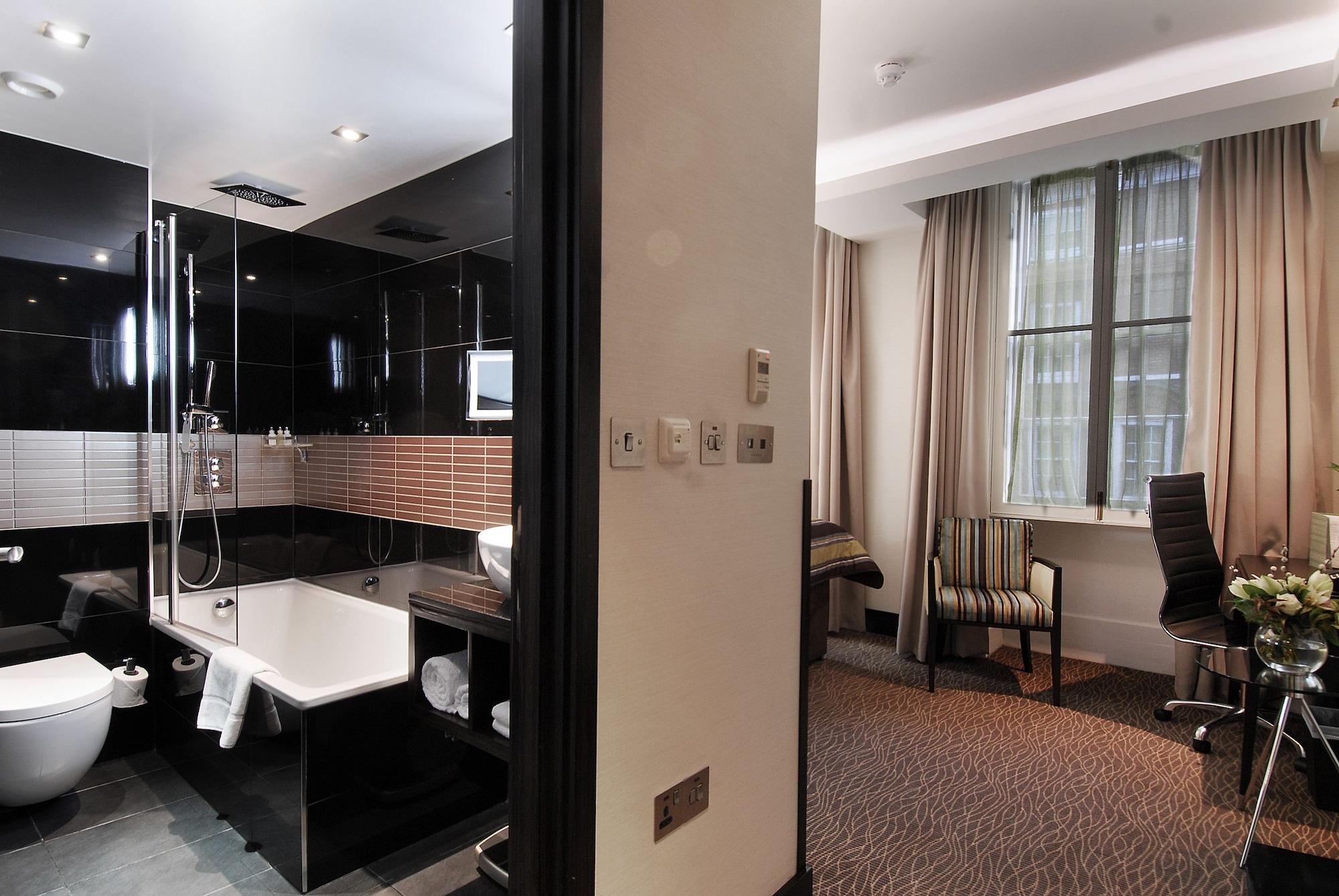 Отель Montcalm Brewery Townhouse Лондон Экстерьер фото The photo shows a modern hotel room that features an elegant bathroom on one side and a living area on the other. 

1. **Bathroom**: The bathroom is stylishly designed with a combination of black and white tiles. It includes a bathtub, a shower area 