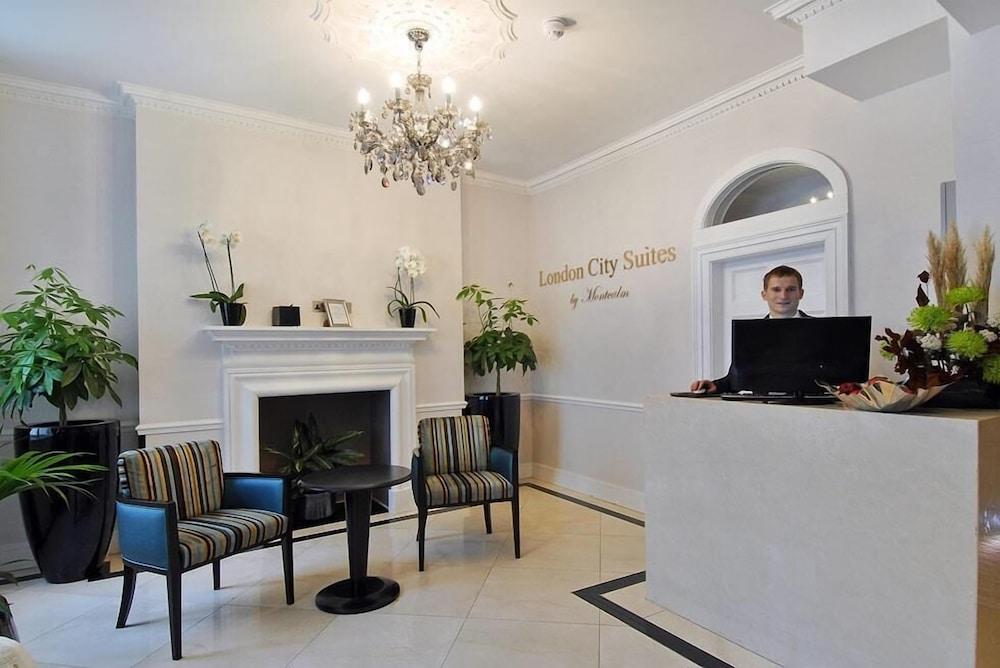 Отель Montcalm Brewery Townhouse Лондон Экстерьер фото The photo shows the interior of a reception area in a hotel called "London City Suites." The space features a light-colored wall with the hotel's name displayed. There is a stylish chandelier hanging from the ceiling, providing warm lighting. 

In th