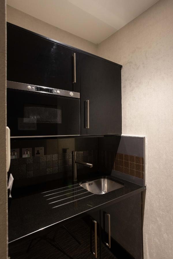 Отель Montcalm Brewery Townhouse Лондон Экстерьер фото The photo shows a modern kitchen setup with a dark color scheme. It features:

- A built-in microwave oven situated above a countertop.
- A sleek black cabinet beneath the microwave, which likely stores kitchen items.
- A stainless steel sink placed 