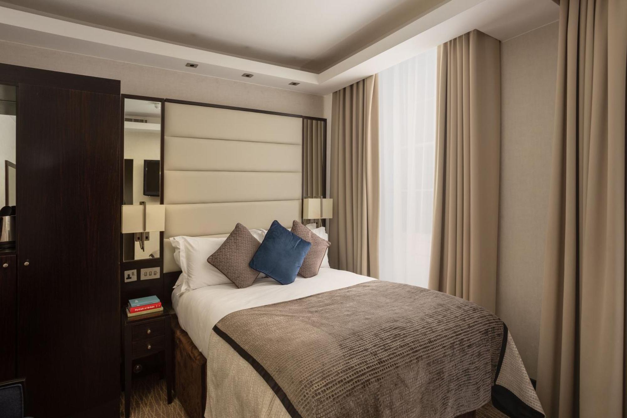 Отель Montcalm Brewery Townhouse Лондон Экстерьер фото The photo shows a modern hotel room with a cozy design. It features a double bed with a light-colored headboard and a soft, stylish blanket. There are decorative pillows on the bed, including a blue one. On either side of the bed, there are small nig