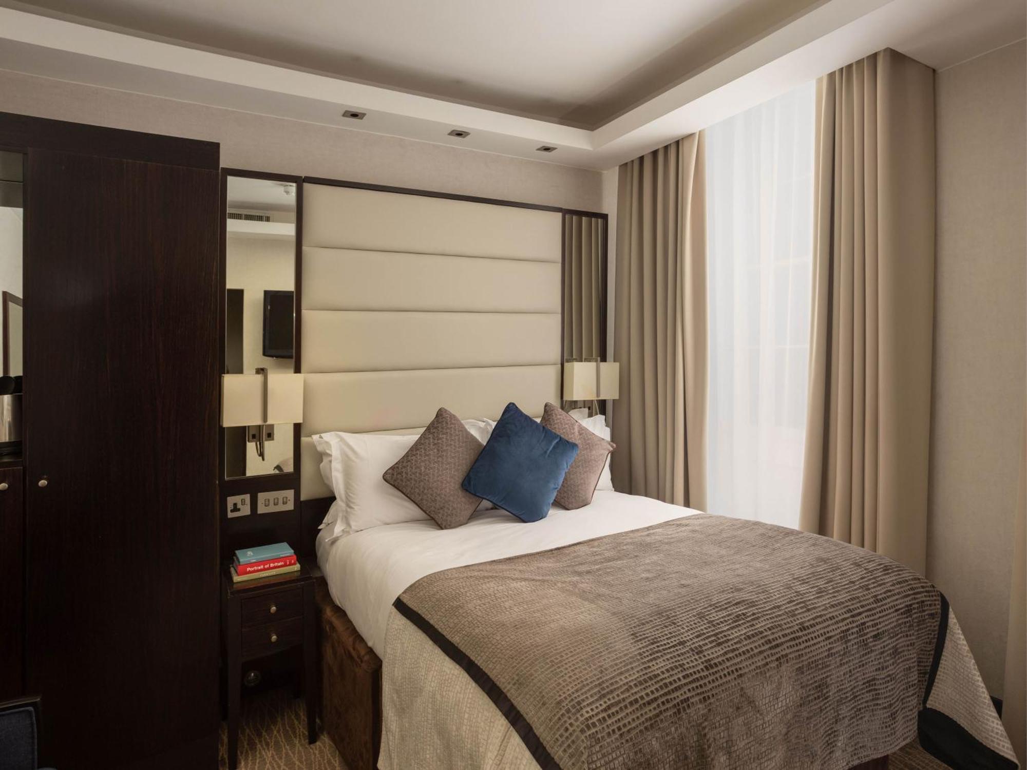 Отель Montcalm Brewery Townhouse Лондон Экстерьер фото The image shows a cozy bedroom. It features a comfortable double bed with a light-colored duvet and decorative pillows in shades of blue and gray. The headboard is upholstered in a soft material, and there are bedside lamps on either side of the bed.