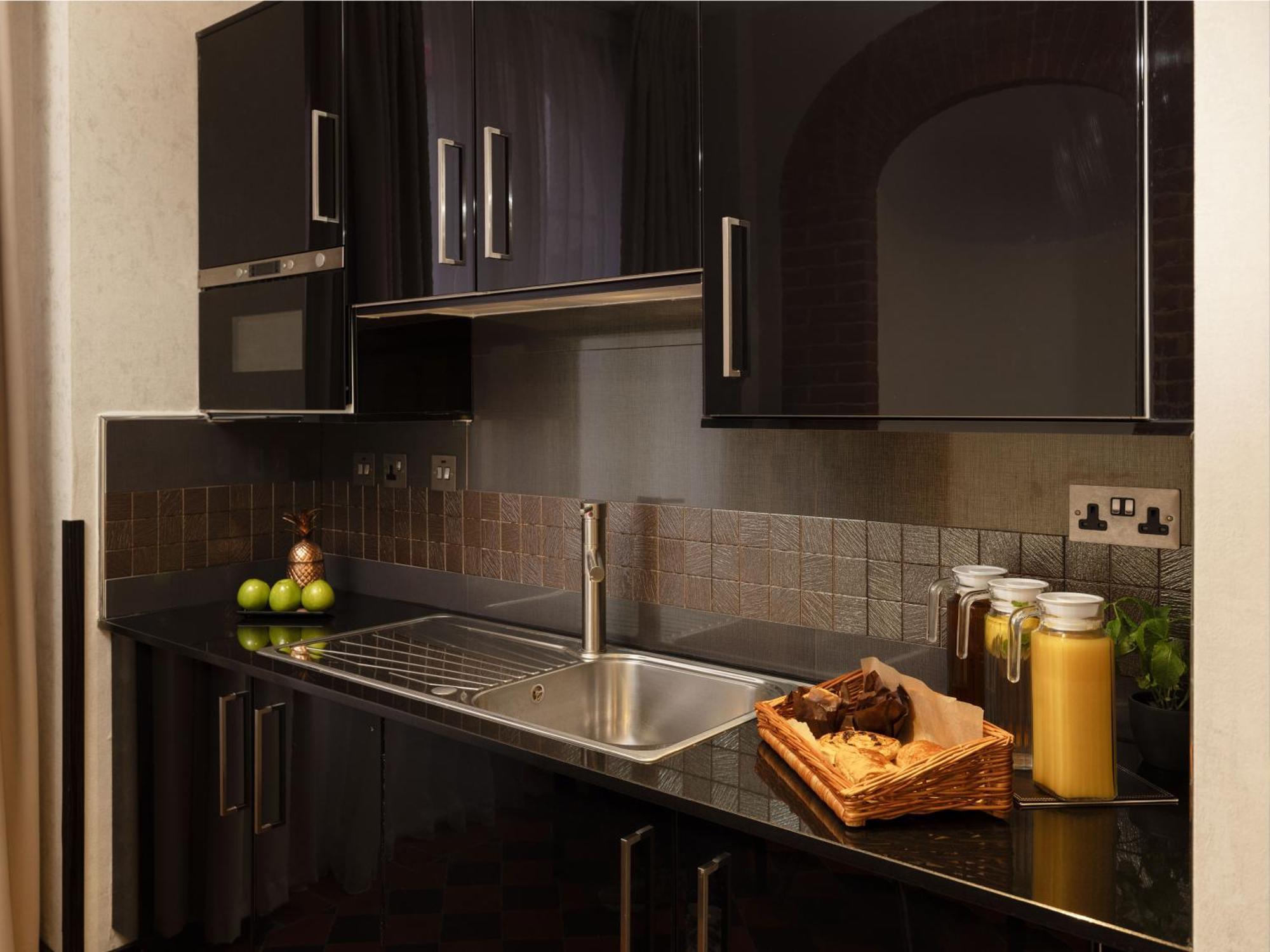 Отель Montcalm Brewery Townhouse Лондон Экстерьер фото The photo shows a modern kitchen with sleek black cabinetry and a glossy finish. The kitchen features a stainless steel sink with a contemporary faucet, set against a dark, textured countertop. Above the counter, there are cabinets that match the cou
