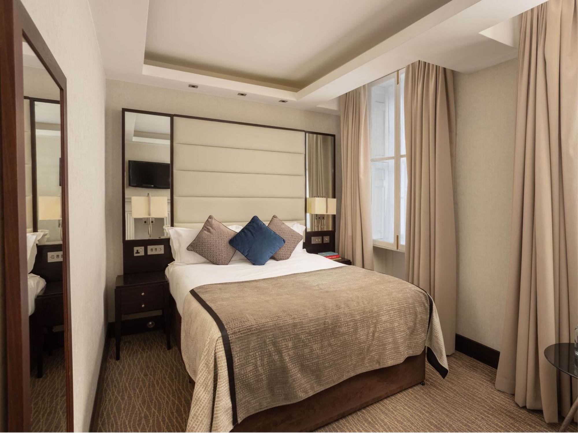 Отель Montcalm Brewery Townhouse Лондон Экстерьер фото The photo shows a cozy hotel room with a bed as the focal point. The bed is made with neutral-colored linens and has several pillows, including a decorative blue one. There are bedside tables on either side of the bed, each with a lamp. A large mirro