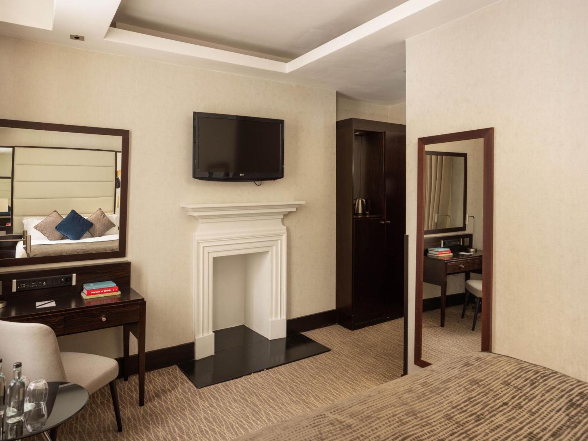 Отель Montcalm Brewery Townhouse Лондон Экстерьер фото The photo depicts a stylish hotel room. It features a double bed, a large flat-screen TV mounted on the wall, and a decorative fireplace. There is a wooden desk with a chair beside it, as well as a mirror hanging on the wall. The decor is modern and 