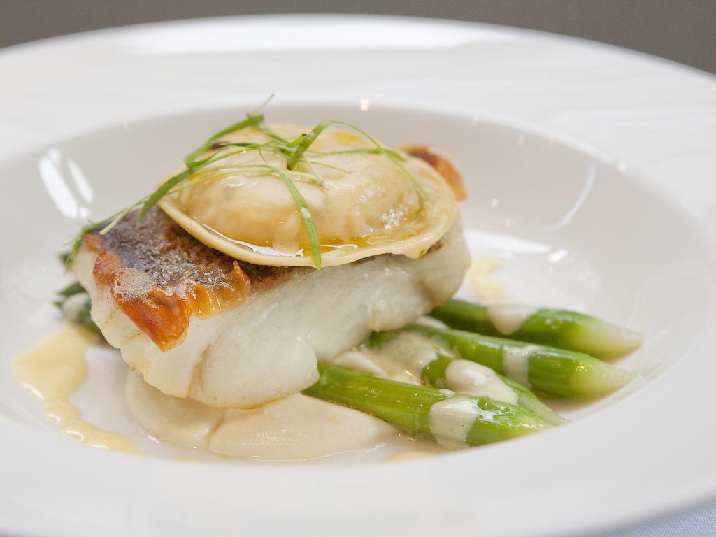 Отель Montcalm Brewery Townhouse Лондон Экстерьер фото The image shows a beautifully presented dish featuring a piece of fish, likely a white fish, topped with a clam. It is served on a bed of green asparagus spears. The dish is garnished with thinly sliced herbs or greens, adding a touch of color. The s