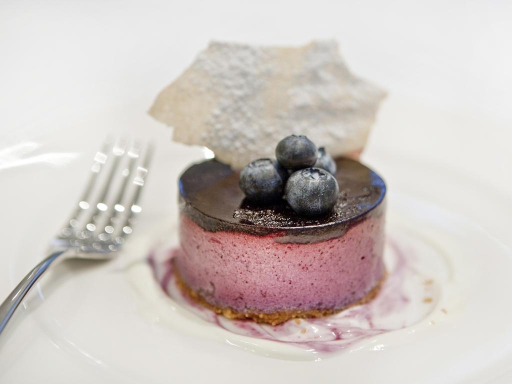 Отель Montcalm Brewery Townhouse Лондон Экстерьер фото The photo shows a beautifully plated dessert, which appears to be a round cheesecake or mousse. It has a pinkish-purple filling, topped with a glossy dark chocolate layer. Three fresh blueberries sit on top, adding a pop of color. The dessert is acco