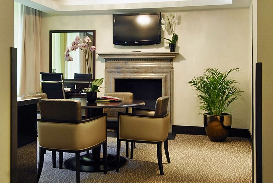 Отель Montcalm Brewery Townhouse Лондон Экстерьер фото The photo shows a modern and stylish room with a dining or meeting area. There is a round table surrounded by four upholstered chairs. A flat-screen television is mounted on the wall above a decorative fireplace. To the side, there is a mirror reflec