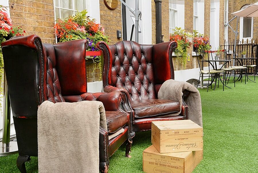 Отель Montcalm Brewery Townhouse Лондон Экстерьер фото The photo depicts two large, elegant armchairs with a classic design, featuring rich burgundy leather upholstery and button tufting. They are positioned in a cozy outdoor setting, with lush green artificial grass beneath them. Next to the chairs, the